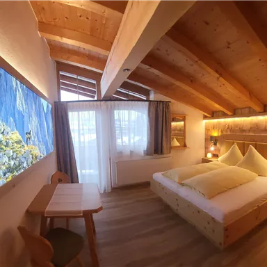 Ein gemütliches Schlafzimmer mit Holzwänden und einem großen Bett. Große Fenster lassen viel Licht herein und bieten einen Blick nach draußen.