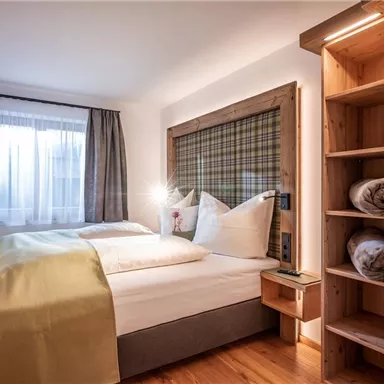 A modern bedroom with a double bed and wooden shelves. Bright curtains and a warm color scheme create a cozy atmosphere.