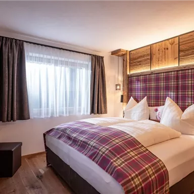 A cozy bedroom with a large bed and checkered pillows. The room has wooden paneling and a window with curtains that lets in natural light.