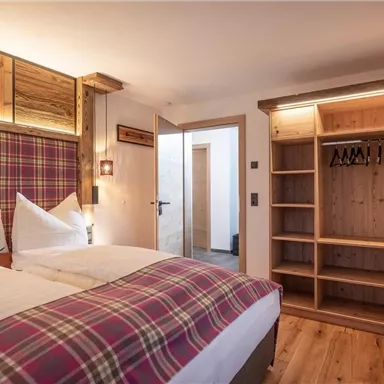 A cozy bedroom with a double bed and modern wooden furniture. The room has a warm, inviting character with an open wardrobe.