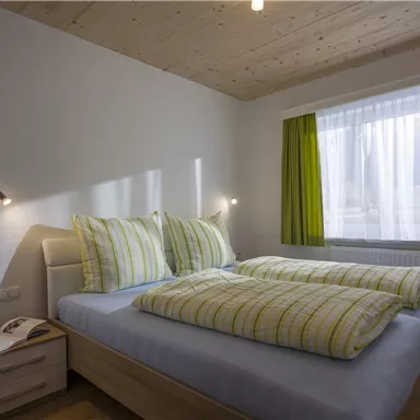 Ein gemütliches Schlafzimmer mit einem großen Bett und frischen, gestreiften Bettdecken. Die Fenster sind mit grünen Vorhängen dekoriert und der Raum hat eine helle, freundliche Atmosphäre.