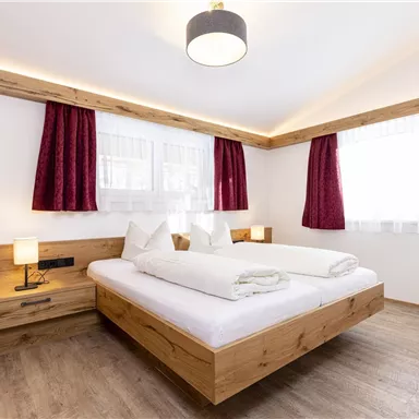 Ein gemütliches Schlafzimmer mit einem Doppelbett und modernen Holzmöbeln. Die großen Fenster lassen viel Tageslicht hereinfalten.