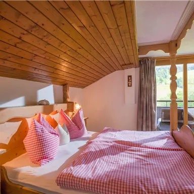 Ein gemütliches Schlafzimmer mit Holzvertäfelung und rot-weiß karierten Kissen. Es gibt einen Balkon mit Blick auf die Natur.