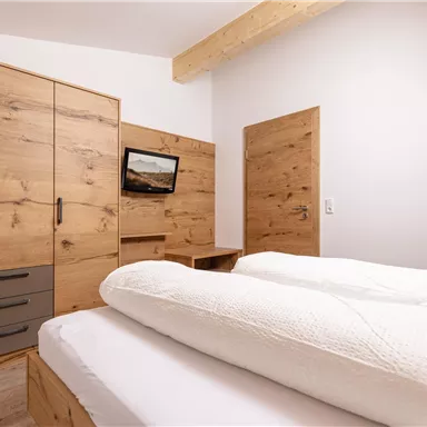 Ein modernes Schlafzimmer mit Holzschränken und einem Doppelbett. An der Wand hängt ein Fernseher, und die Wände sind hell gestrichen.