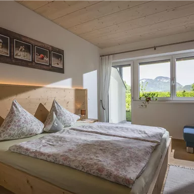 Ein helles und modernes Schlafzimmer mit einem Doppelbett und Bildern an der Wand. Große Fenster bieten einen Blick auf die Berge und die Natur draußen.