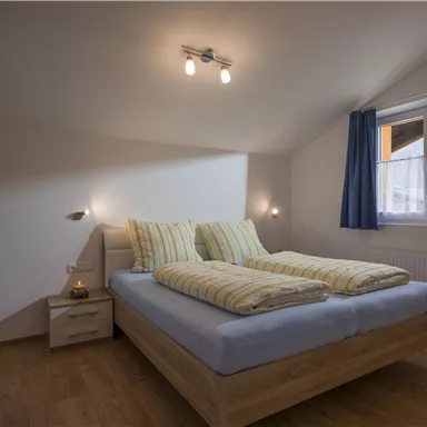 Ein gemütliches Schlafzimmer mit einem Doppelbett und hellen Bettdecken. Tageslicht fällt durch das Fenster und sorgt für eine einladende Atmosphäre.