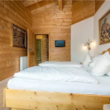 Ein gemütliches Schlafzimmer mit Holzwänden und zwei Betten. An der Wand hängt ein Gemälde, und es gibt einen kleinen Fernseher.