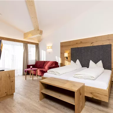 Ein gemütliches Schlafzimmer mit zwei Betten und Holzdetails. Es gibt eine rote Couch und einen Fernseher in der Ecke.