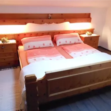 Ein gemütliches Schlafzimmer mit einem Holzbett und sanfter Beleuchtung. Die Bettwäsche ist in sanften Farben gehalten und es gibt Nachttische auf beiden Seiten.