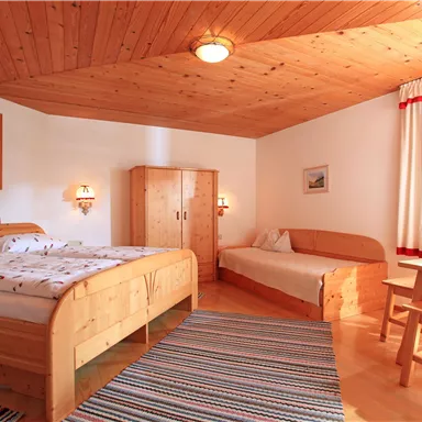 A cozy room with wooden decor, a double bed, and a single bed. The light and the windows create a friendly atmosphere.