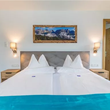 Ein modernes Schlafzimmer mit einem Doppelbett und hellblauen Akzenten. An der Wand hängt ein Landschaftsgemälde, und der Raum ist gut beleuchtet.