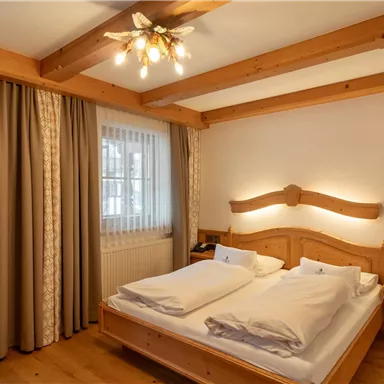 Ein gemütliches Schlafzimmer mit einem Doppelbett und Holzverkleidung. Große Fenster lassen viel Licht herein und es gibt beige Vorhänge.