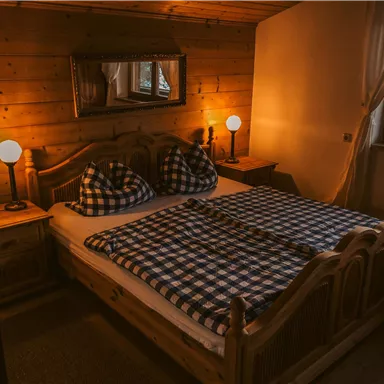 Ein gemütliches Schlafzimmer mit einem Holzbett und karierten Bettdecken. Das warme Licht der Lampen schafft eine einladende Atmosphäre.