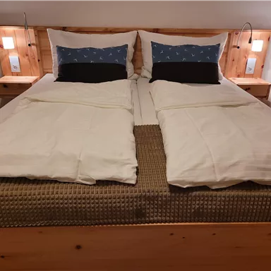 Ein gemütliches Schlafzimmer mit einem großen Bett und zwei Kissen. Die Wände sind hell und es gibt Nachtlichter an den Seiten.
