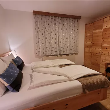 Ein gemütliches Schlafzimmer mit einem großen Bett und holzfarbigen Möbeln. Die Fenster sind mit Vorhängen verhangen, und es gibt eine kleine Sitzecke im Raum.