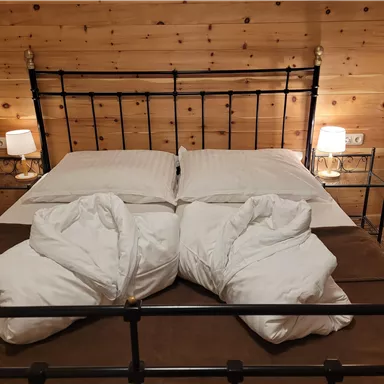 Ein gemütliches Schlafzimmer mit einem Metallbett und zwei Kissen. Die Holzwände und die sanften Lichter schaffen eine einladende Atmosphäre.