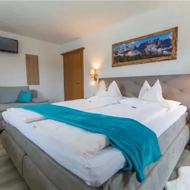 Ein modernes Schlafzimmer mit einem großen Doppelbett und weißen Bettwäsche. An der Wand hängt ein Bild, und es gibt eine gemütliche Sitzecke mit einem Sofa.