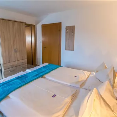 Ein helles Schlafzimmer mit zwei Betten und moderner Einrichtung. Es gibt einen Kleiderschrank und einen Nachttisch neben dem Bett.