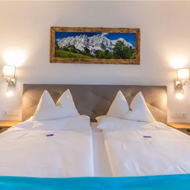 Ein gemütliches Schlafzimmer mit zwei getrennten Betten und eleganter Bettwäsche. An der Wand hängt ein schönes Bild von Bergen.