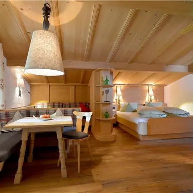 Ein gemütlicher Raum mit Holzverkleidung und einem Esstisch. Im Hintergrund befindet sich ein Bett und eine warme, einladende Atmosphäre.