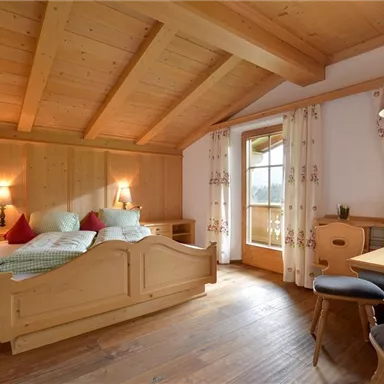 Ein gemütliches Schlafzimmer mit Holzwänden und einem großen Bett. Es gibt einen Essbereich mit einem Tisch und Stühlen sowie große Fenster, die natürliches Licht hereinlassen.