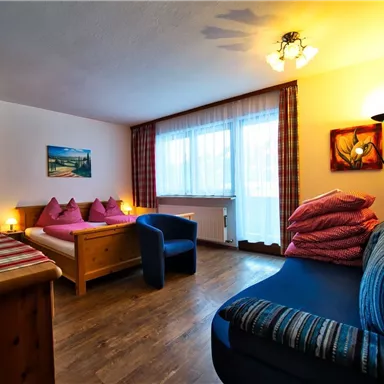 Ein gemütliches Zimmer mit einem Sofa und einem Holzschrank. Es gibt zwei Fenster mit Vorhängen und eine warme Beleuchtung.