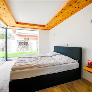 Ein modernes Schlafzimmer mit einem großen Bett und einer minimalistischen Einrichtung. Die großen Fenster bieten Blick auf den Garten und sorgen für viel Tageslicht.