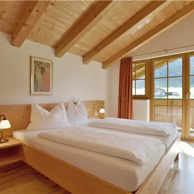 Ein gemütliches Schlafzimmer mit Holzdecke und großen Fenstern. Die Einrichtung ist hell und einladend, ideal für einen entspannenden Aufenthalt.