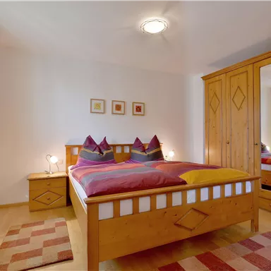 Ein gemütliches Schlafzimmer mit einem Doppelbett und bunten Kissen. Der Raum ist hell und einladend mit einem Holzschrank und einem Teppich.