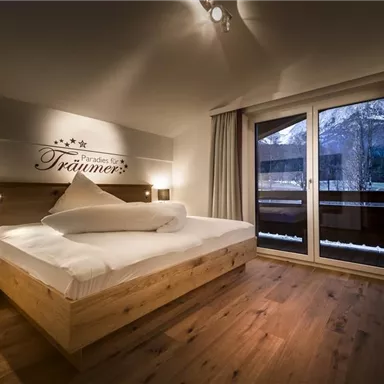 A cozy bedroom with a modern wooden bed and a view of the balcony. The warm colors and soft lines create an inviting atmosphere.