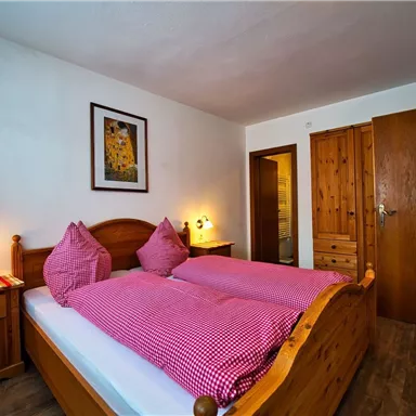 Ein gemütliches Schlafzimmer mit einem Doppelbett und karierten Kissen. Die Wände sind hell und das Zimmer hat Holzdetails sowie ein Fenster mit Aussicht.