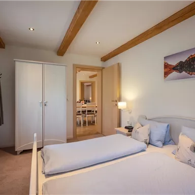 Ein gemütliches Schlafzimmer mit einem Doppelbett und hellen Wänden. Das Zimmer enthält einen Kleiderschrank und ein Bild an der Wand.