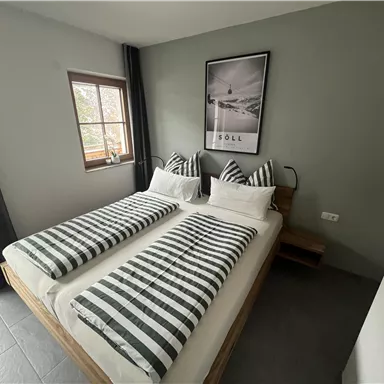 A modern bedroom with two single beds and striped bed covers. The room has large windows and a calm color scheme.