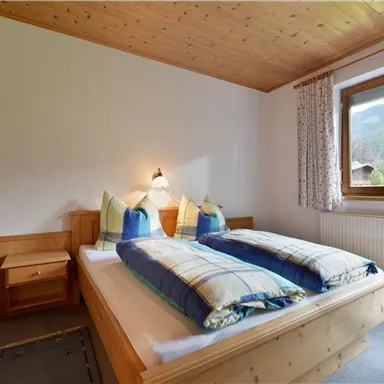 A cozy bedroom with two beds and wooden furniture. The room has a window with a view of the mountains and offers a bright, inviting atmosphere.