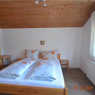A simple bedroom with a double bed and two nightstands. The wooden walls and the window create a cozy atmosphere.