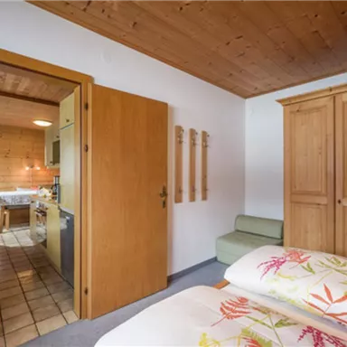 A cozy room with two beds and colorful bedspreads. In the background, you can see an open kitchen and living area.