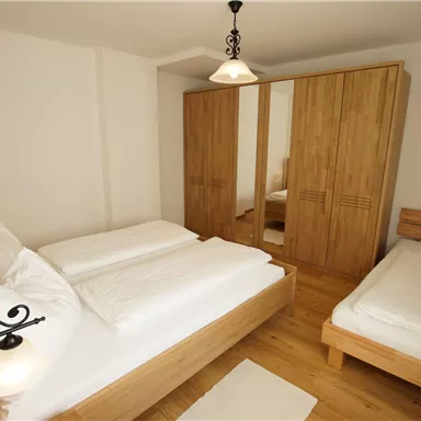 Ein helles Schlafzimmer mit Holzmöbeln und zwei Betten. Im Raum steht ein Kleiderschrank und ein großer Spiegel.