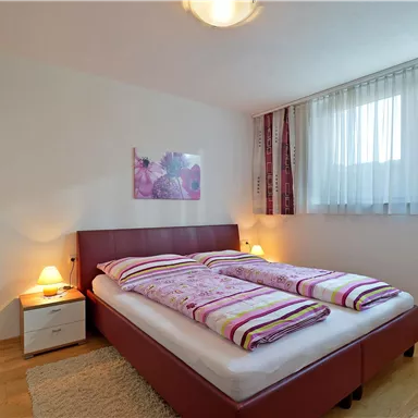 Ein gemütliches Schlafzimmer mit einem Doppelbett und weißen Bettwäsche. Das Zimmer hat große Fenster, die viel Licht hereinlassen.