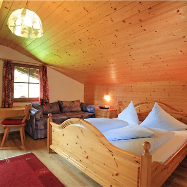 Ein gemütliches Schlafzimmer mit Holzverkleidung und großen Fenstern. Das Zimmer enthält ein Doppelbett, eine Couch und Holzmöbel.