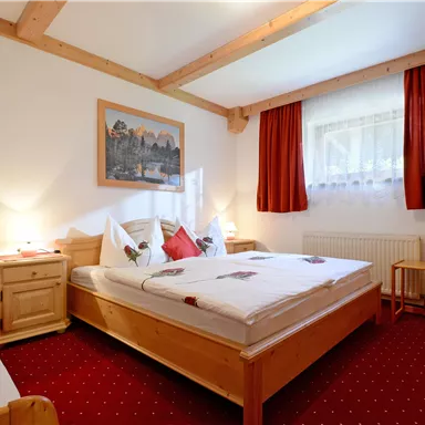 Ein gemütliches Schlafzimmer mit zwei Betten und hellen Holzmöbeln. Der Raum hat rote Vorhänge und ein schönes Bild an der Wand.