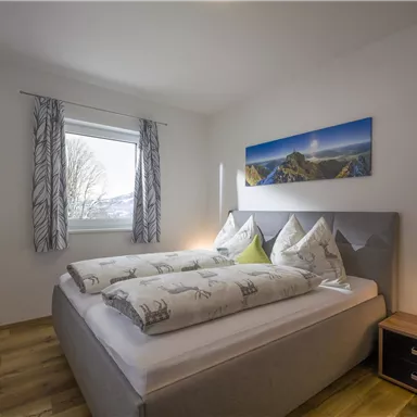 A cozy bedroom with a double bed and soft colors. The window lets in a lot of light and there is a beautiful picture above the bed.