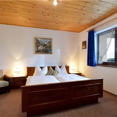 Ein gemütliches Zimmer mit zwei Betten und Holzdecke. Die Fenster sind mit blauen Vorhängen dekoriert.