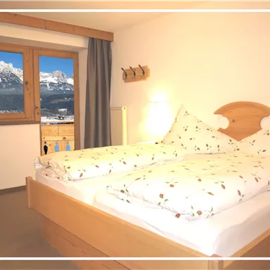 Ein gemütliches Schlafzimmer mit zwei Betten und Blumenbettwäsche. Der Blick aus dem Fenster zeigt beeindruckende Berge und eine klare Aussicht.