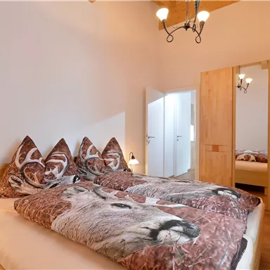 Ein gemütliches Schlafzimmer mit einem Doppelbett und Fellen mit Tiermotiven. Es gibt einen Kleiderschrank und einen großen Spiegel, die für genügend Stauraum sorgen.