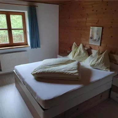 Ein gemütliches Schlafzimmer mit einem großen Bett und zwei Kissen. Das Holzdesign und das Fenster sorgen für eine einladende Atmosphäre.
