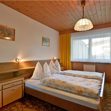 Ein gemütliches Schlafzimmer mit zwei Betten und hellen Vorhängen. Die Wände sind in warmen Tönen gehalten und es gibt eine angenehme Atmosphäre.