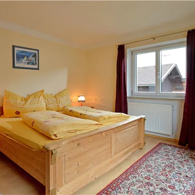 Ein gemütliches Schlafzimmer mit einem Doppelbett und zwei Nachtischen. Es hat helle Wände, ein Fenster mit Vorhängen und einen Fernseher.