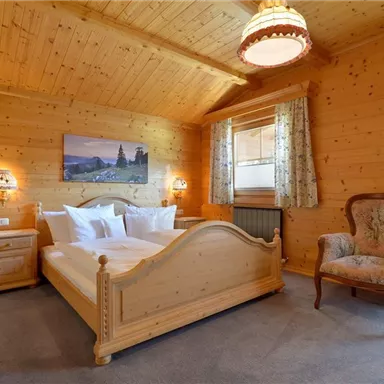 Ein gemütliches Schlafzimmer mit Holzwänden und einem großen Bett. An den Fenstern hängen Vorhänge und es gibt einen bequemen Sessel.