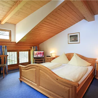 Ein gemütliches Schlafzimmer mit Holzvertäfelung und einem großen Doppelbett. Der Raum verfügt über ein Fenster mit Blick nach draußen und einen kleinen Tisch mit Stühlen.