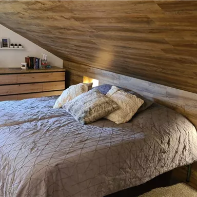 A cozy bedroom with a large bed and modern wood decor. On the wall, there are bedside lamps and personal items.